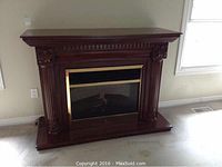 Front view of Dimplex electric fireplace in decorative dark wood mantel with ornate column details and brass trim.