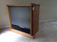 Full view of the large 60" Mitsubishi projection TV housed in an oak-like wooden cabinet on casters, showing front and side views.