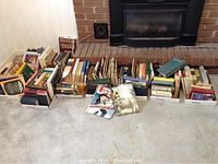 Full view of multiple boxes and stacks of assorted books, mostly hardback and some paperbacks, various genres including novels, reference, travel, and religious texts.