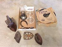 Photo showing two early flat irons, a metal trivet, the 11-inch oil lamp, glass candle holders, and a box of early photo albums.