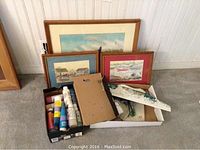 Three framed watercolours leaning against wall with paint supplies and model boat