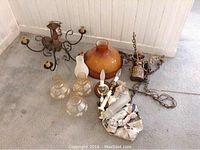 Full view of 5-branch brass hanging light fixture, glass chimneys, porcelain candle lights, and large amber glass shade on floor.