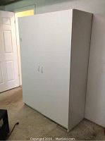 Exterior view of the white cabinet with closed double doors, positioned against a wall in a room with a beige carpet.