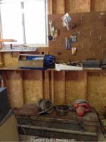 Wide view of workshop with wooden shelves, pegboard with hanging tools, tile cutter on wooden supports, power tools on workbench, and wooden box on floor.