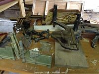Photo showing various metal mitre boxes and adjustable angle tools on wooden surface, tools show signs of rust and wear.