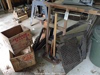 Overview of two wooden crates, cast iron grates, stove rings, hand cart and axes