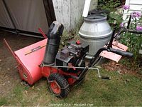 Side view of the snow blower showing housing, engine, tires and chute assembly