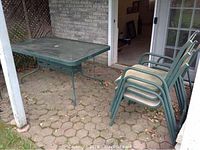 Photo of rectangular glass top patio table with metal frame and four stacked matching patio chairs with beige cushions.