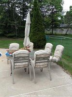 Overall view of the rectangular patio table with six chairs and closed white umbrella on an outdoor concrete patio with greenery in background.