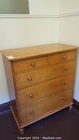 Front view of a vintage wooden dresser showing five drawers and round wooden knobs, positioned in a corner against walls.