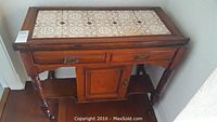 Front and side view showing overall vintage hall table with tile inset top, turned legs, drawers, and cabinet door.