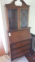 Full front view of the vintage secretary hutch showing glass cabinet, slant desk front, and drawers.