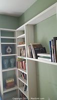 White built-in shelves holding a wooden mantel clock, two blue ceramic bust vases, and books.