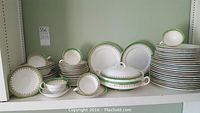Full view of the Aynsley bone china set including stacked plates, bowls, cups, saucers and covered serving bowl on shelf.
