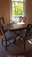 Table and four chairs near window showing overall size and style, visible crack on one table leg.