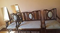 Three-piece set of vintage wooden seating: one bench with oval upholstered back insert and two matching armchairs with similar design and upholstery.