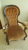 Full front view of the vintage wooden arm chair showing carved details and upholstered seat and back in brownish velvet fabric.