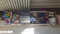 Wide view of the lot showing 8 boxes with assorted items including ribbons, purses, bone china pieces, and decorative figurines.
