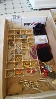 Wide view of box containing organized jewelry tray with multiple compartments holding earrings, bracelet, and other costume jewelry items.