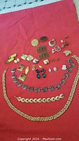 Full view of jewelry pieces laid out on red fabric background showing earrings, necklaces, and brooches.