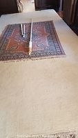 Large white wool rug under smaller area rug with a white curtain rod placed on top, showing overall condition and size context