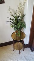 Brass table with two tiers and artificial plant placed on top.
