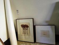 Photo showing two framed prints leaning against wall with rolled white poster tube beside.