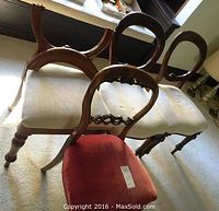 Four wooden balloon back chairs, three with white cushions and one with a red cushion, arranged on carpet. One chair is facing forward showing the balloon back design.