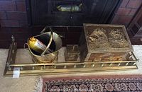 Full view of the brass fireplace fender with the brass wood storage box, brass bucket, and smaller brass box arranged on it in front of a fireplace.