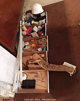 Overview of boxes containing assorted tools, white hard hat on top, wooden boomerang, and craft materials.