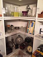 Corner shelf with various glass vases, metal meat grinders, vintage Columbia dial scale, and books visible.