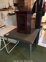 Solid wood antique corner display cabinet with glass door on foldable card table in room.