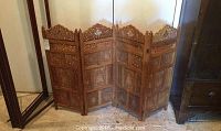 Full view of the four-panel carved wooden screen standing on floor