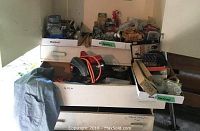 Wide view showing the assortment of hardware boxes, nails, hooks, electrical supplies, and the Skilsaw with extension cords placed on top of a wooden box.