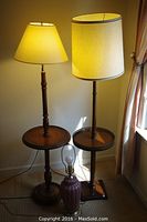 Full view showing two tall wooden table lamps standing side by side with beige lampshades and a shorter mauve ceramic lamp in front.