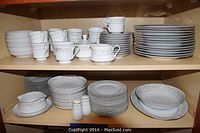 Full shelf display showing stacks of Royal Wentworth china: multiple plates of various sizes, cups, saucers, cream and sugar bowl, salt and pepper shakers, and gravy boat, all with matching floral pattern and silver trim.