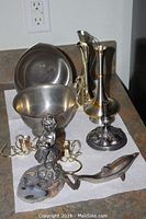 Photo showing various pewter and metal decorative items including bowls, a statue, candlestick, and bottles opener