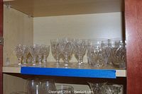 Full view of two rows of etched stemmed cordial glasses and rock glasses arranged on a shelf.