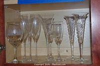 Photo of variety of eight stemmed glasses displayed in cabinet, including the twisting lattice stem champagne flutes and decorative wine glasses with gold or silver accents