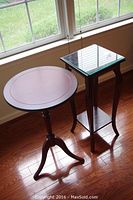 Photo of two mahogany plant stands near window; one square with beveled glass top, one round with visible wear