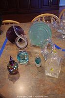Overview of various art glass perfume bottles and decorative glass items on table
