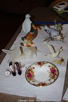 Overall view of seven bird figurines and a small floral dish on a white cloth surface