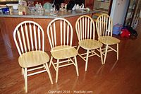 Set of four natural wood dining chairs arranged in a row on a hardwood floor, showing overall condition and design.