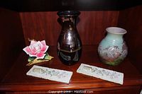 Wide shot showing all five items: porcelain rose, two vases, and two ceramic plaques arranged on a wooden shelf