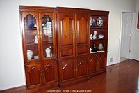 Full view of the three wooden entertainment center units combined against a wall, showing upper glass door cabinets, paneled storage doors, and open shelving.