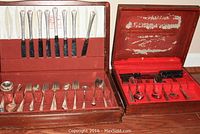 Overview of two opened wooden flatware boxes showing full sets of knives, forks, spoons, and serving pieces in fabric-lined compartments.