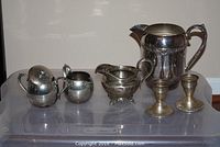 Full set of silver plated items including sugar bowl, creamer, two pitchers, and two candlesticks on plastic storage bin.