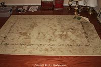 Photo of one Latte pattern area rug from Somerset Collection laid on hardwood floor, showing worn floral leaf border pattern and beige background.