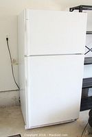 Full exterior view of white Kenmore top freezer refrigerator plugged in and closed.