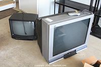 Two CRT televisions on floor, a silver Panasonic 32 inch TV with remote on top, and a smaller black Sharp TV at the back.